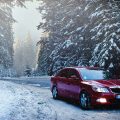 red car on a snowy road driving amid forest