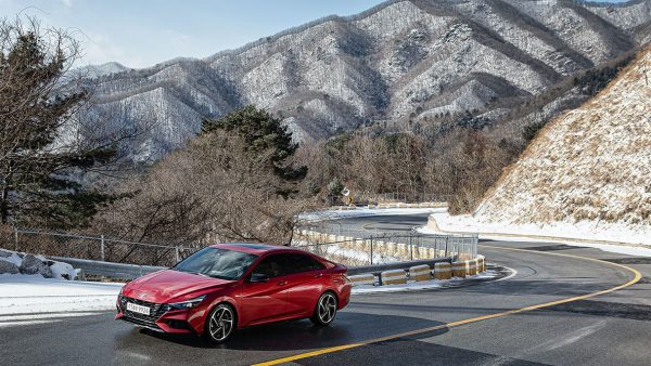 red hyundai driving on windy road, mountain in back